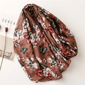 Gros plan d'une écharpe marron aspect lin avec motifs papillons et fleurs sur fond blanc