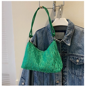 Close-up of emerald green pleated fabric texture and sleek strap on a crescent bag