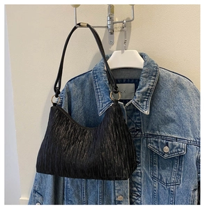 Detail of black pleated hobo bag showing wavy fabric texture and gold hardware ring