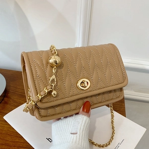 Quilted khaki crossbody bag with gold chain and metal sphere detail on a magazine