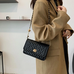 Quilted black leather crossbody bag with gold chain strap shown on model's shoulder