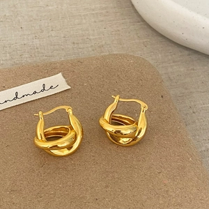 Gros plan de boucles d'oreilles créoles dorées avec un design entrelacé poli sur tissu
