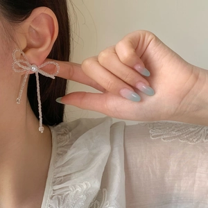 Elegant white crystal bow earrings with tassel fringe worn by a model in close-up view
