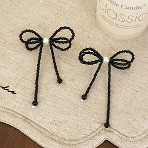 Detail of elegant black beaded bow earrings with white pearls and hanging tassels
