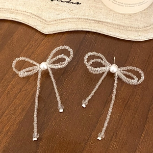 Handmade beaded bow earrings with white tassels on a rustic wooden table setting