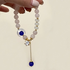 Handheld display of a pink quartz beaded bracelet with crescent moon and crystal charms