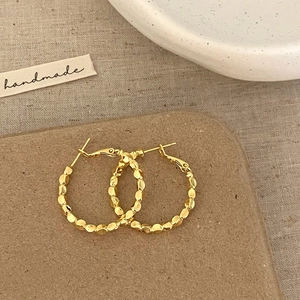 Detailed view of gold hoop earrings with textured beaded surface on linen background