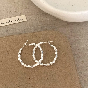 Macro detail of textured silver hoop earrings with hammered finish on a neutral fabric