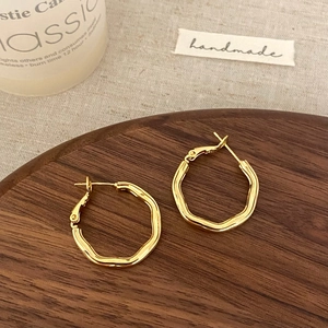 Macro detail of gold irregular geometric earrings on a wooden tray with warm lighting