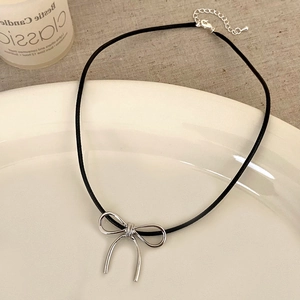 Minimalist silver bow pendant necklace on black cord cord presented in a white ceramic dish