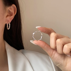 Polished silver textured hoop earrings with a faceted metallic finish worn by a model