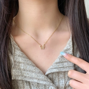 Elegant gold butterfly pendant necklace with zircon pavé worn by a model on a knitted top