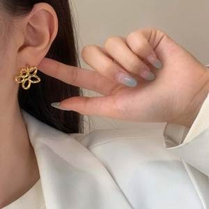 Close-up of minimalist gold hollow flower earrings on model with elegant white blazer