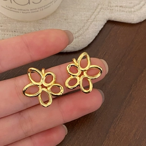 Detailed view of gold hollow flower earrings held by hand to show polished floral design