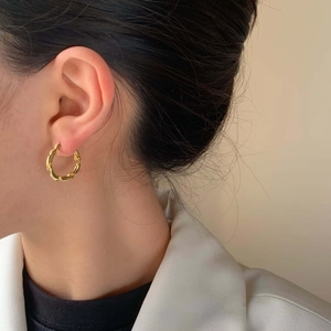 Elegant gold twisted hoop earrings with a textured weave design worn by a model