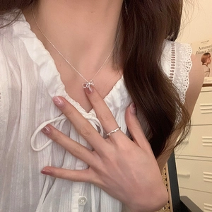 Elegant silver bow pendant necklace and branch ring worn with a white blouse