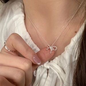 Detail of silver bow pendant necklace and textured ring on model with soft lighting