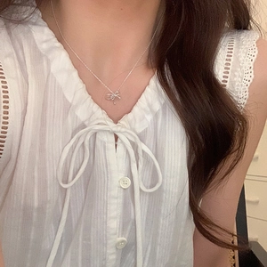 Detail of silver bow pendant necklace worn by a model in a white lace shirt