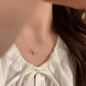 Close-up of a silver bow pendant necklace worn on a white textured blouse