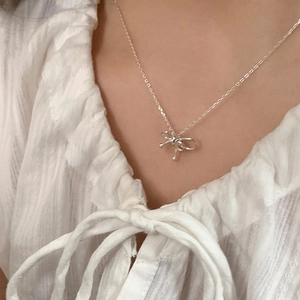 Close-up of a silver bow necklace on a white shirt showing sweet minimalist style