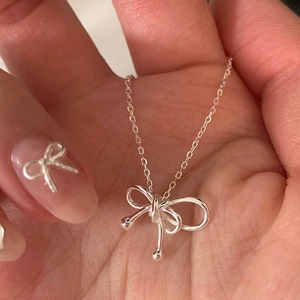 Close-up of a silver bow pendant necklace with a delicate chain held in hand