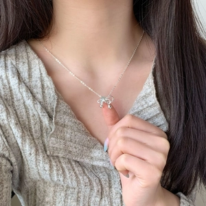 Close-up of a delicate silver bow pendant necklace worn by a model on the neck