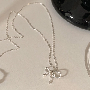 Close-up of a silver bow necklace pendant on a minimalist cream textured background