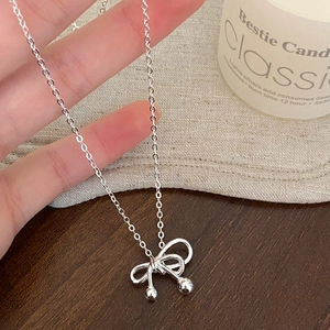 Close-up of a silver bow necklace with metal beads on a rustic wooden and linen background