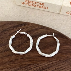 Macro shot of matte silver twisted hoop earrings on a dark wooden display tray