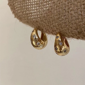 Close-up of gold hoop earrings with starburst zircon settings on rustic linen cloth