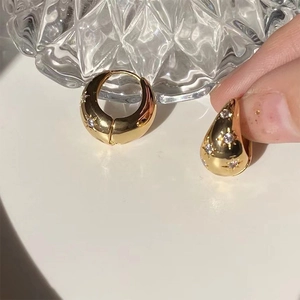 Detail of gold hoop earrings featuring star engravings and embedded zircon stones