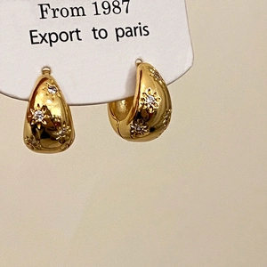 Macro detail of gold C-shaped earrings with zircon floral patterns on card