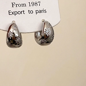 Macro detail of silver huggie earrings featuring embossed floral patterns and cubic zirconia
