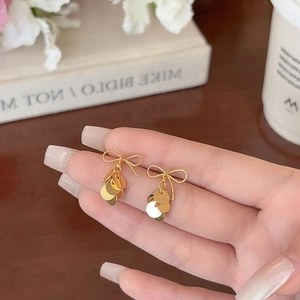 Macro detail of golden bow earrings with shimmering round sequin tassels held by hand