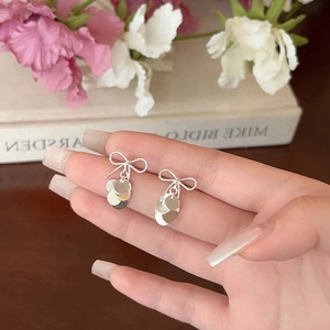 Close-up of silver bow stud earrings with dangling metal sequins held by fingers