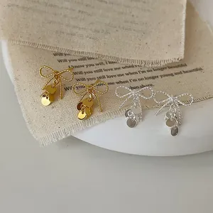 Close-up of bow earrings with hanging metal sequins in gold and silver finish