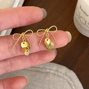 Close-up of golden bow-knot earrings with sequin tassels and twisted metal texture
