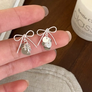 Macro shot of silver bow knot earrings with dangling sequins and twisted texture detail