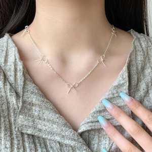 Silver dainty chain necklace featuring five minimalist metal bow pendants on female model