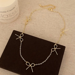 Macro detail of golden bow necklace featuring twisted rope textures and lobster clasp