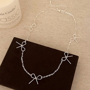 Close-up of five silver bow pendants with rope texture on a delicate metal chain