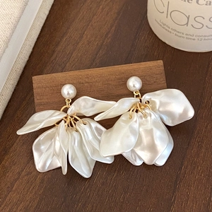 Detailed macro view of white pearl petal earrings on a dark textured wood background