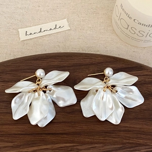 Close-up of white petal tassel earrings with pearls on a wooden tray with soft lighting