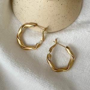 Close-up of matte gold twisted rope hoop earrings on minimalist neutral background