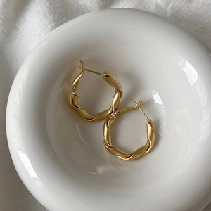 Detail of matte gold twisted rope hoop earrings resting on a white ceramic bowl