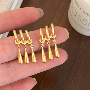 Gros plan de boucles d'oreilles franges dorées avec des finitions mates et des pendentifs