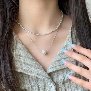 Close-up of double-layer silver chain necklace with elegant white pearl pendant on model