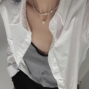 Close-up of double-layered silver necklace with pearl pendant on model wearing white shirt