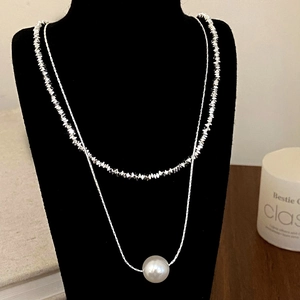 Detail of layered silver necklace with irregular silver flakes and a white pearl pendant
