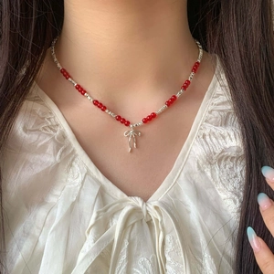 Detail of red beaded necklace with silver bow pendant on a model wearing white lace